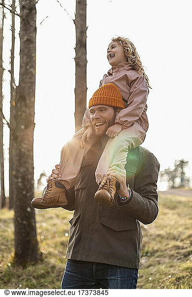 Cheerful father carrying daughter on shoulder at park
