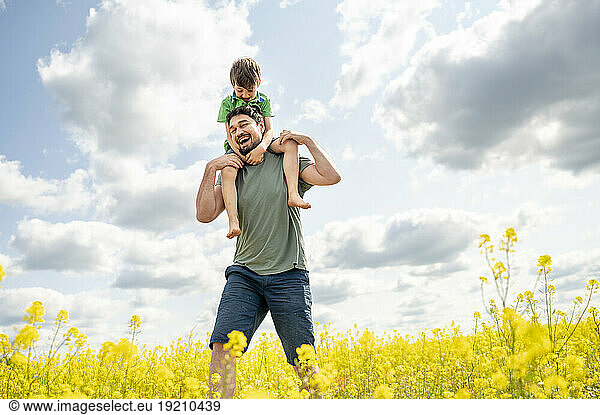 Cheerful father carrying son and walking in field