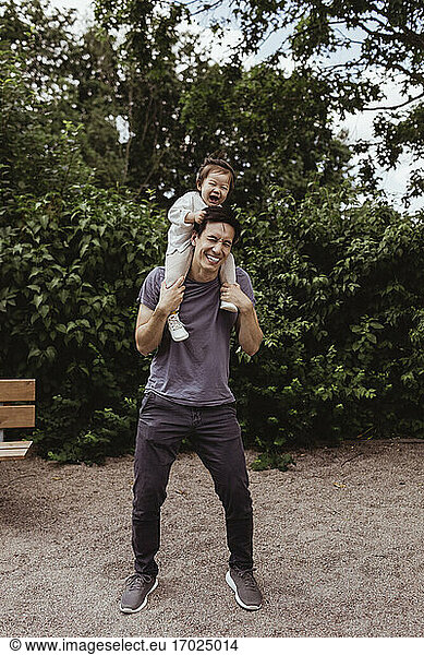 Cheerful father carrying son on shoulder in playground