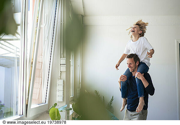 Cheerful father carrying son on shoulders at home
