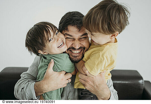 Cheerful father embracing children in front of white wall