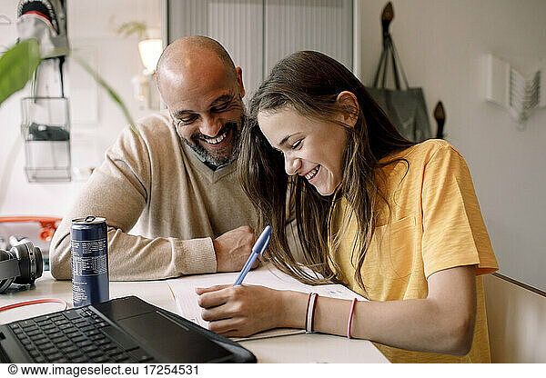 Cheerful father sitting with daughter doing homework while sitting at table
