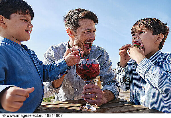 Cheerful father with son eating strawberry on sunny day