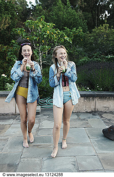 Cheerful female friends dinking juice while walking at poolside