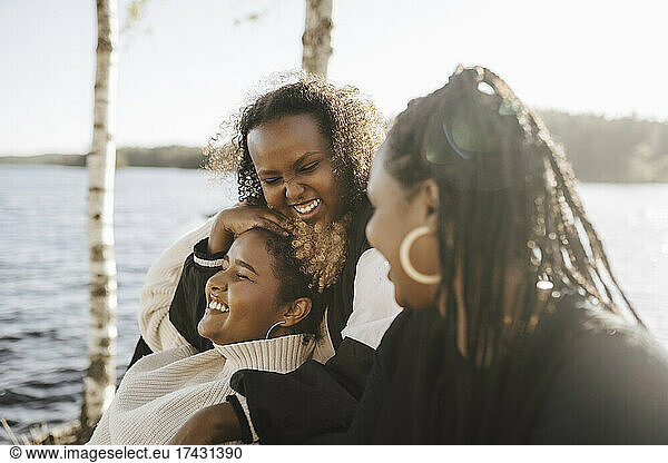 Cheerful female friends enjoying by lake on sunny day