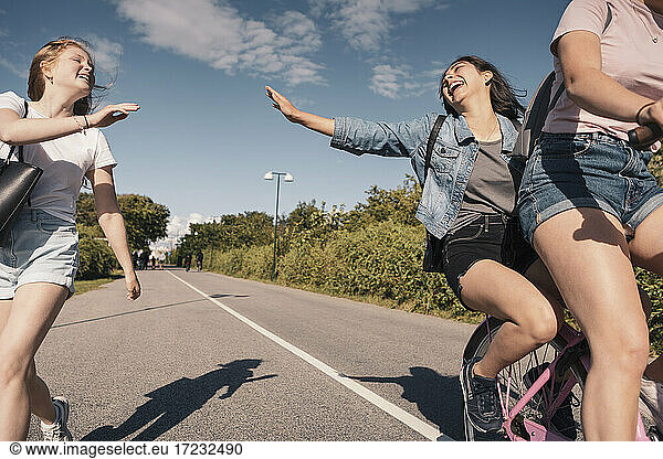 Cheerful female friends enjoying while cycling on road