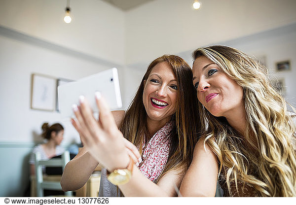 Cheerful female friends taking selfie through smart phone in cafe