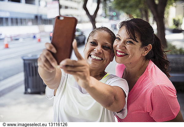Cheerful female friends taking selfie with smart phone on footpath