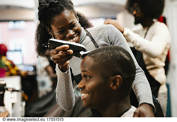 Cheerful female hairdresser cutting hair of male customer with electric razor in barber shop