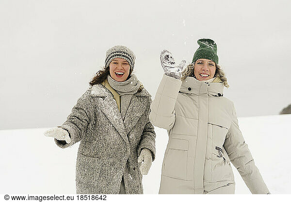 Cheerful friends having fun throwing snow in winter