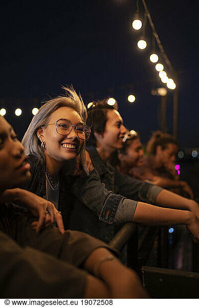 Cheerful friends having social gathering under string lights on rooftop