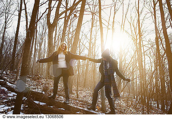 Cheerful friends holding hands while standing on tree trunk