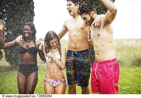 Cheerful friends in swimwear enjoying water spray at yard