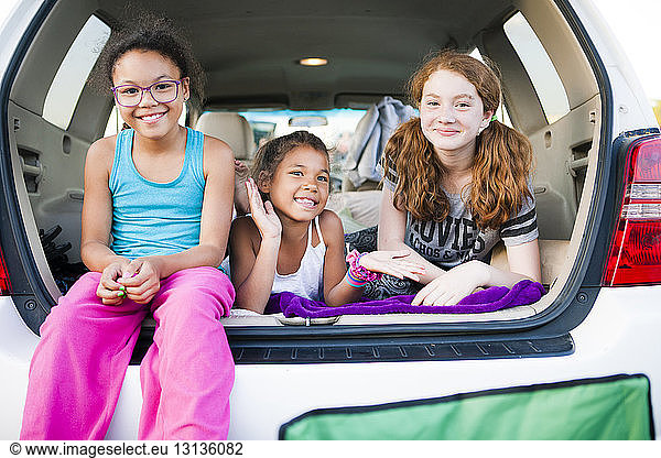 Cheerful friends playing in car trunk
