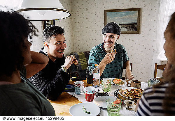 Cheerful friends talking while enjoying food in social gathering at home