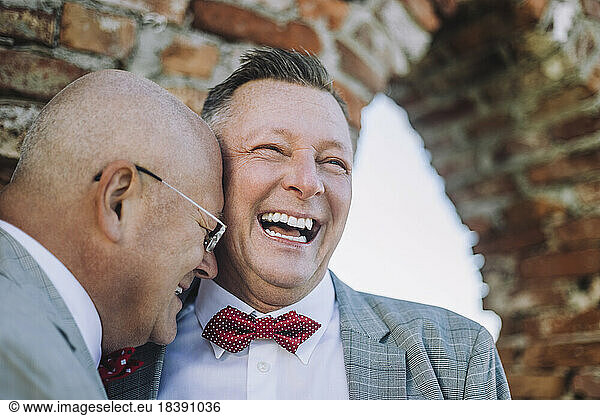 Cheerful gay man laughing with bald partner on wedding day