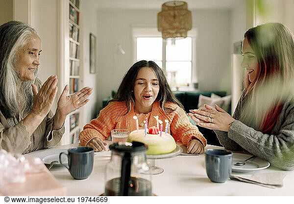 Cheerful girl celebrating birthday with mother and grandmother at home