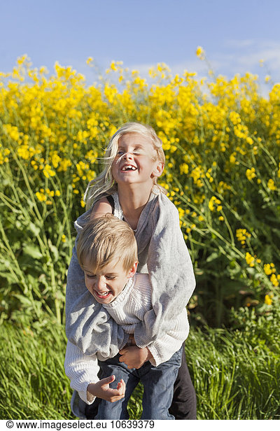 Cheerful girl embracing brother at rapeseed field