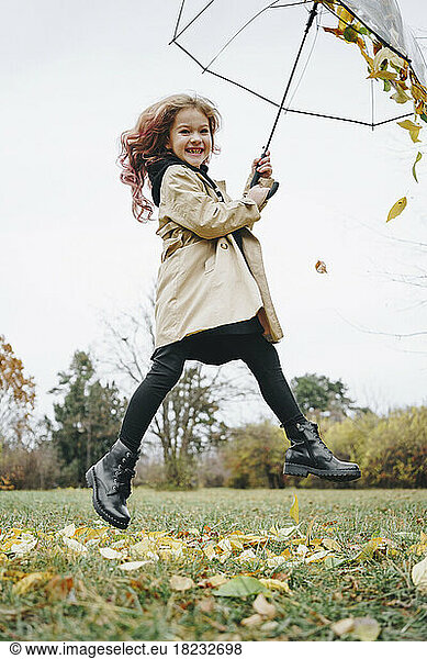 Cheerful girl jumping with umbrella in park