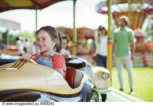 Cheerful girl on carousel in amusement park