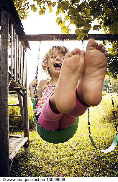 Cheerful girl playing on swing at park