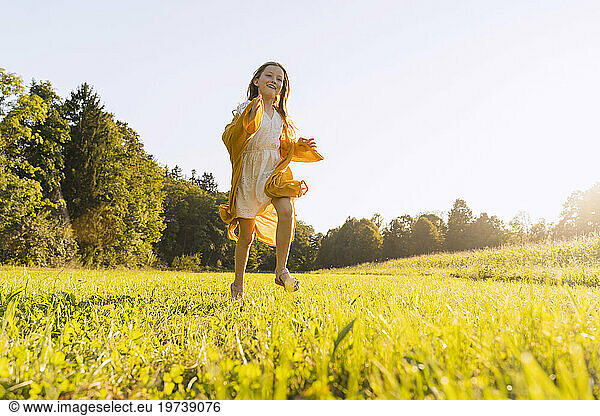 Cheerful girl running on grass in field