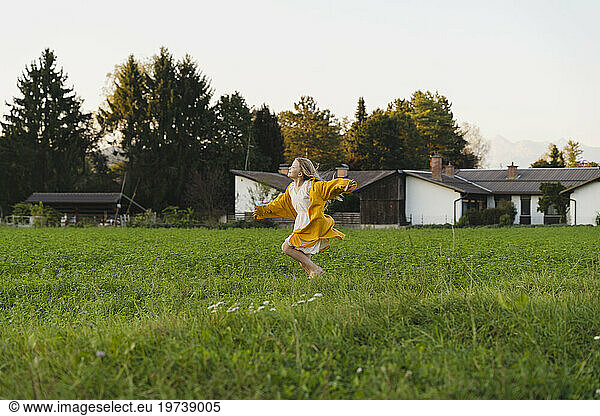 Cheerful girl running on grass in front of houses