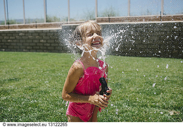 Cheerful girl splashing water on face with garden hose