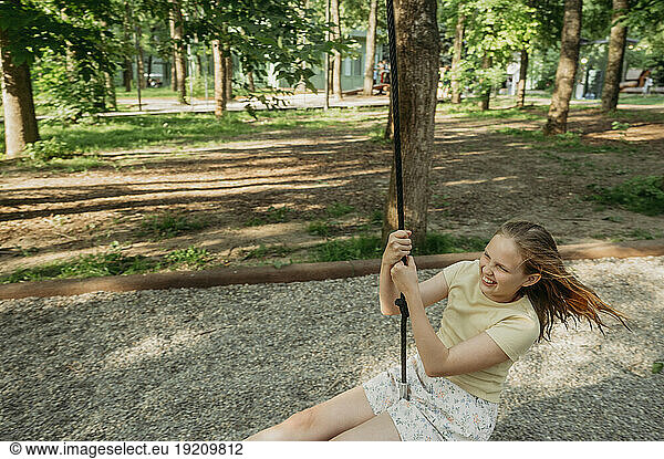 Cheerful girl swinging on swing at park