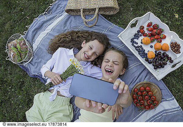 Cheerful girl taking selfie with sister through smart phone in park