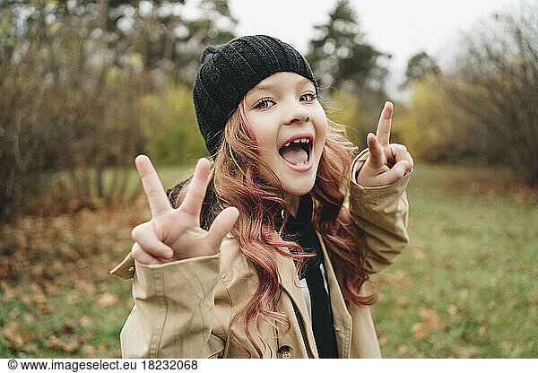 Cheerful girl wearing knit hat showing peace sign gesture in park