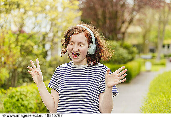 Cheerful girl wearing wireless headphones singing and listening to music