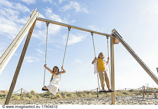 Cheerful girl with brother playing on swing at beach