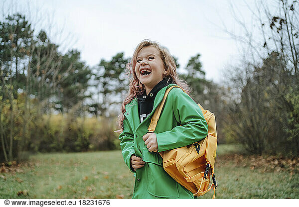 Cheerful girl with yellow backpack standing at park