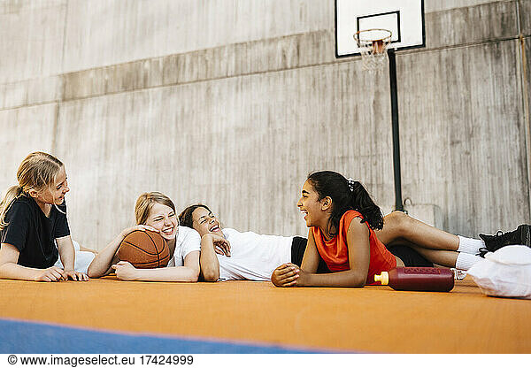 Cheerful girls laughing while lying down at sports court