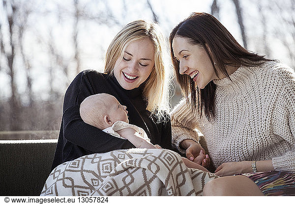 Cheerful homosexual women looking at baby girl in living room