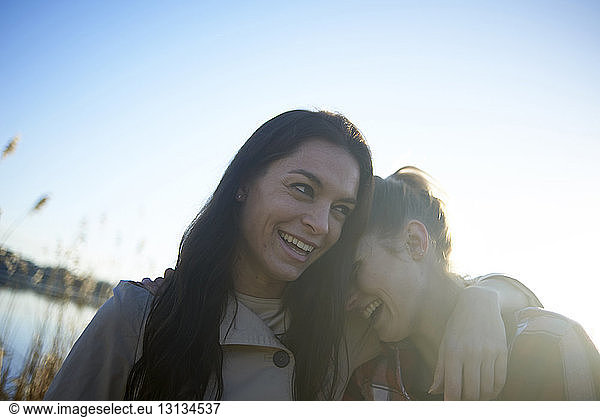 Cheerful lesbian couple against sky during sunset