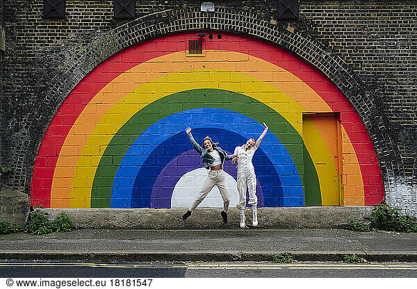 Cheerful lesbian couple jumping in front of mural wall