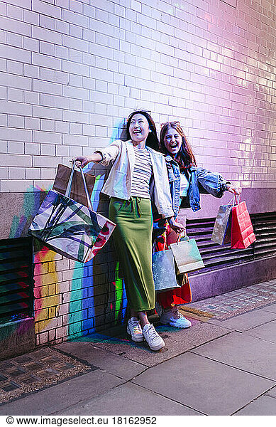 Cheerful lesbian couple with shopping bags by brick wall