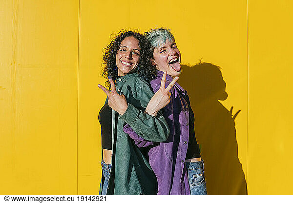 Cheerful lesbian women showing peace sign in front of yellow wall