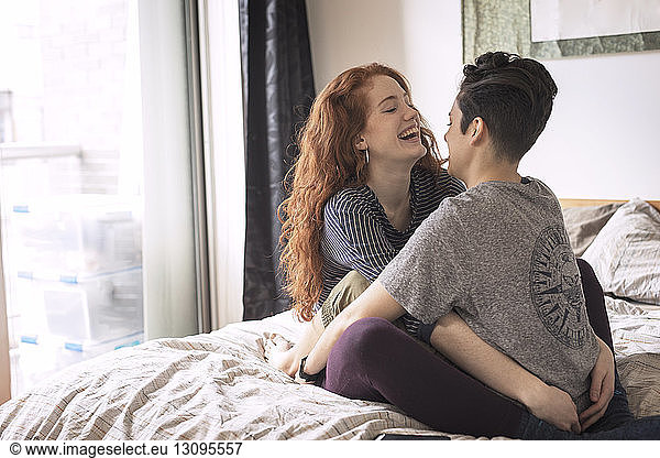Cheerful lesbians sitting face to face on bed at home