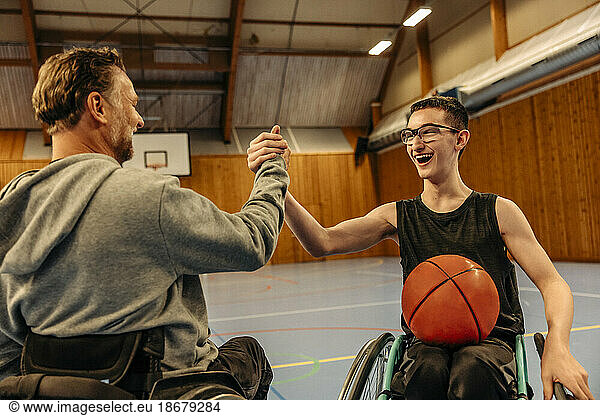Cheerful male and female athletes with disabilities doing handshake while playing basketball at sports court