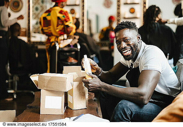Cheerful male barber packaging beauty product in box at hair salon