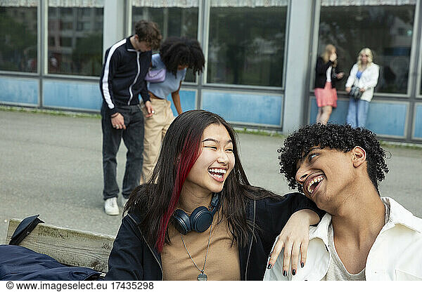 Cheerful male female friends talking while sitting on bench