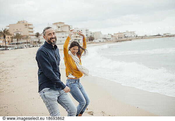 Cheerful man and woman dancing on coastline at beach