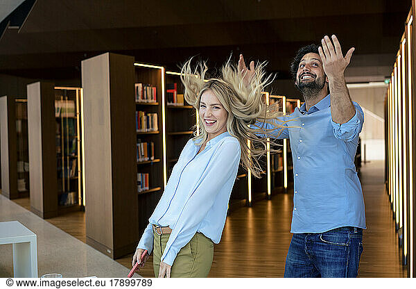 Cheerful man and woman playing in illuminated library
