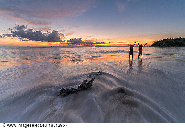 Cheerful man and woman with arms raised at sunset  Caribbean Sea