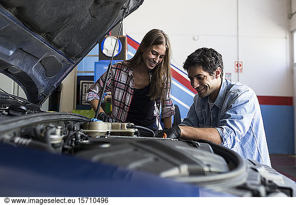 Cheerful man and young woman working together on car repair service and fixing car engine