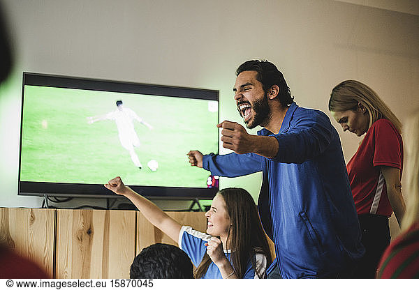 Cheerful man celebrating goal while standing with friends at home
