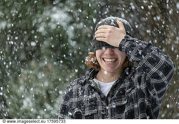 Cheerful man covering eyes with knit hat in snowfall